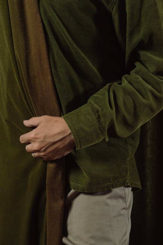 pexels-photo-5044216-5044216 A person wearing a stylish green velvet shirt stands gracefully behind a matching curtain indoors.